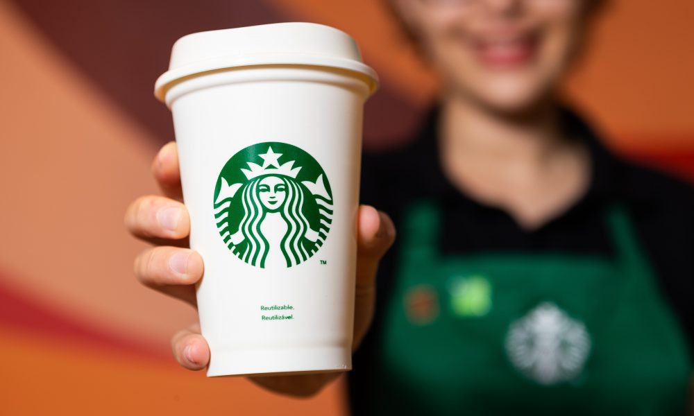 Funcionário da Starbucks, com avental verde segurando um copo de café com a logo da empresa